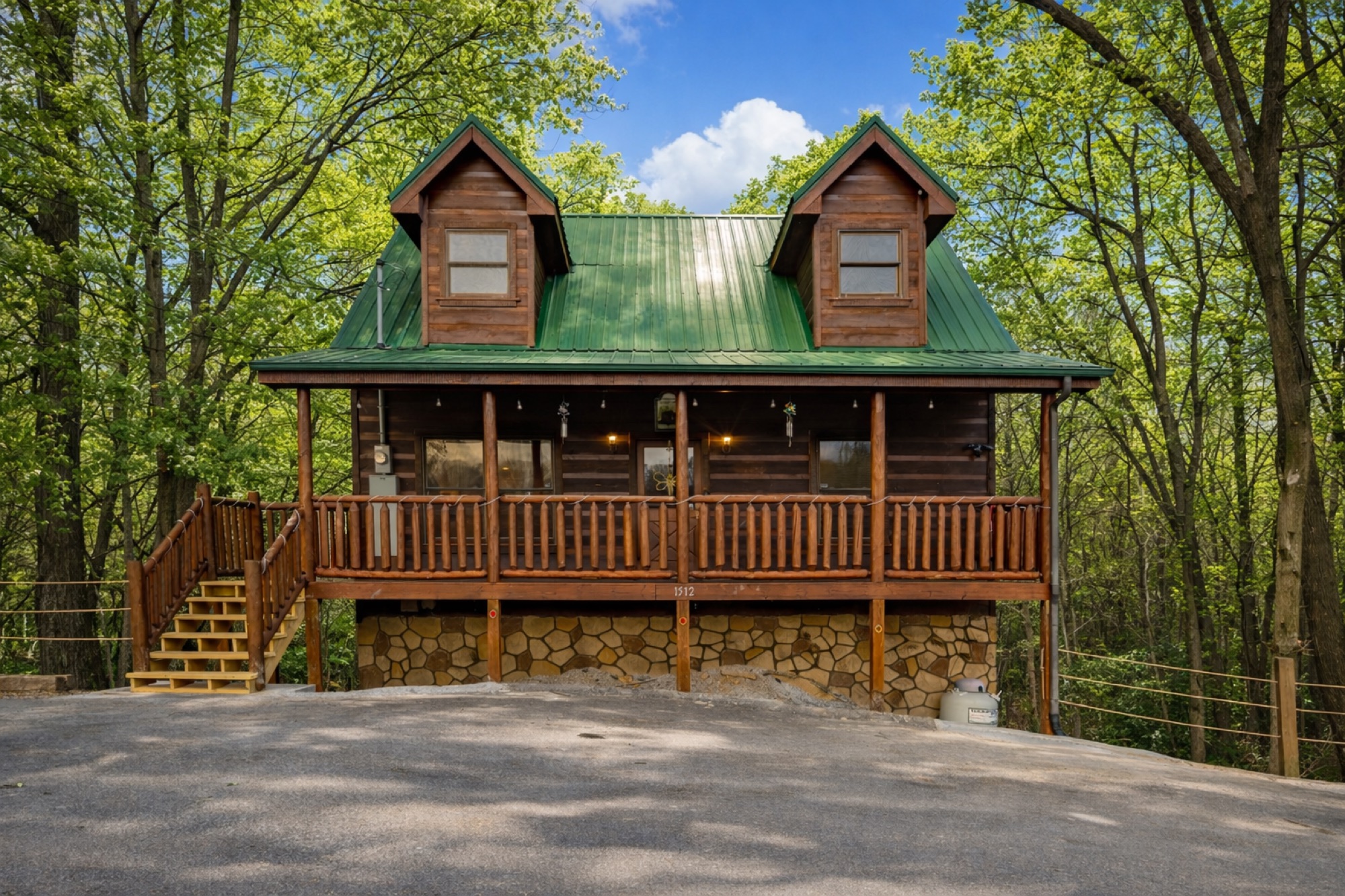 Bearadise log cabin exterior with a green metal roof and covered front porch, surrounded by bright summer greenery